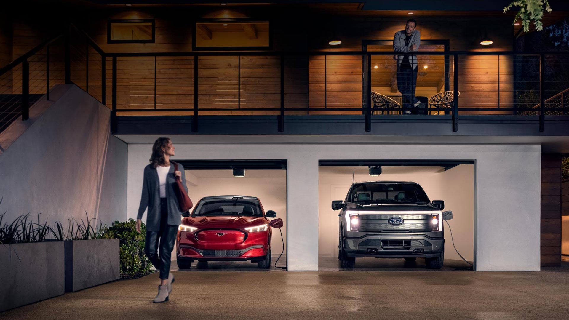 Woman walking out from home garage with a 2024 Mustang® Mach-E and Ford Lightning® truck in plugged-in and charging | Dick's Canby Ford in Canby OR